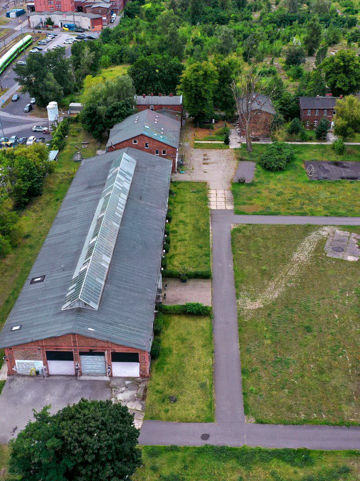 Aerial view of the Cordeshof: the long brick hall with its glass roof, the courtyard, the meadow with concrete pads and the old brick houses among the trees